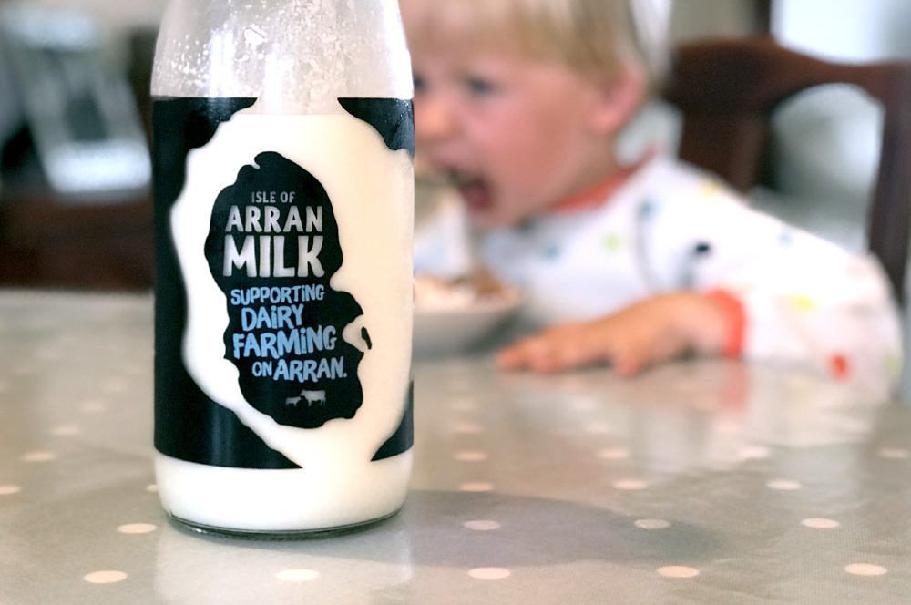 Bottle of Arran Milk in front of a child eating a bowl of cereal